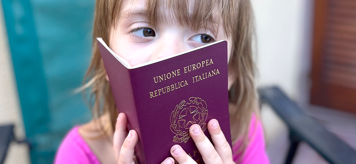 Niña pequeña tapándose la cara con el pasaporte italiano